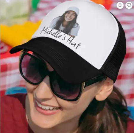 A black and white trucker cap with a custom photo of a woman and the text "Michelle's Hat" printed on the front panel.